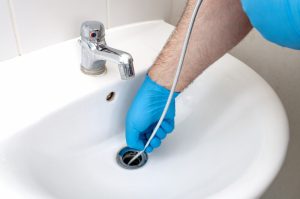 person-with-gloved-hands-using-a-drain-snake-in-a-bathroom-sink